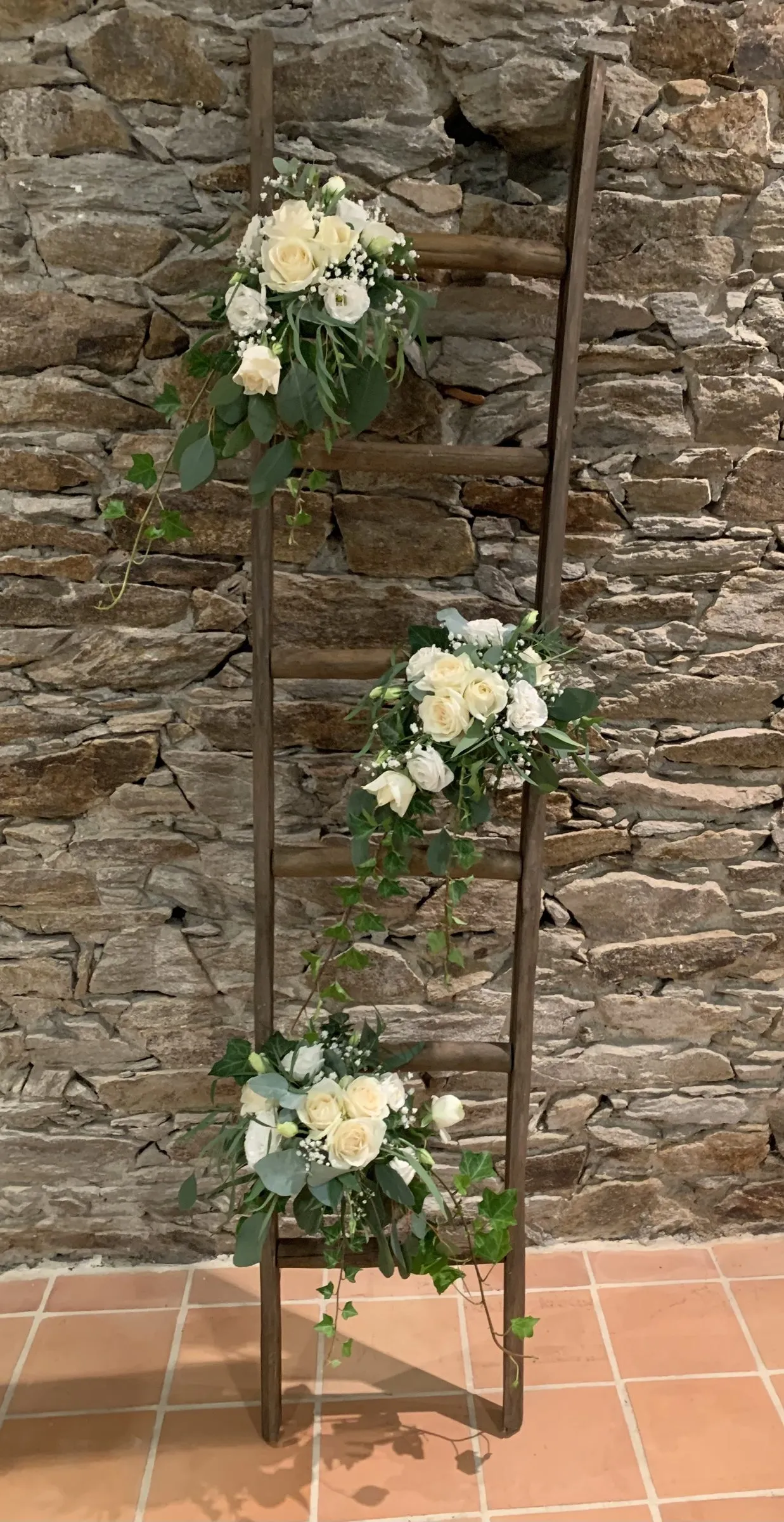 Échelle décorée de roses blanches contre un mur de pierre ancienne