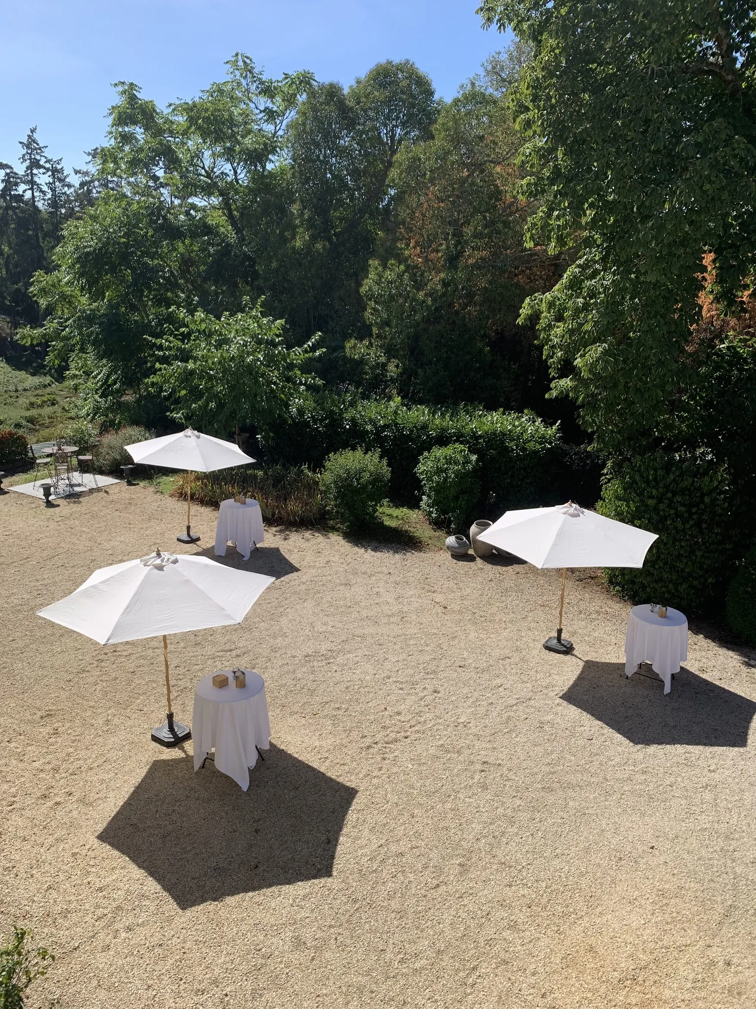 Cocktail dressé dans la cour : parasols et mange-debout sous les arbres