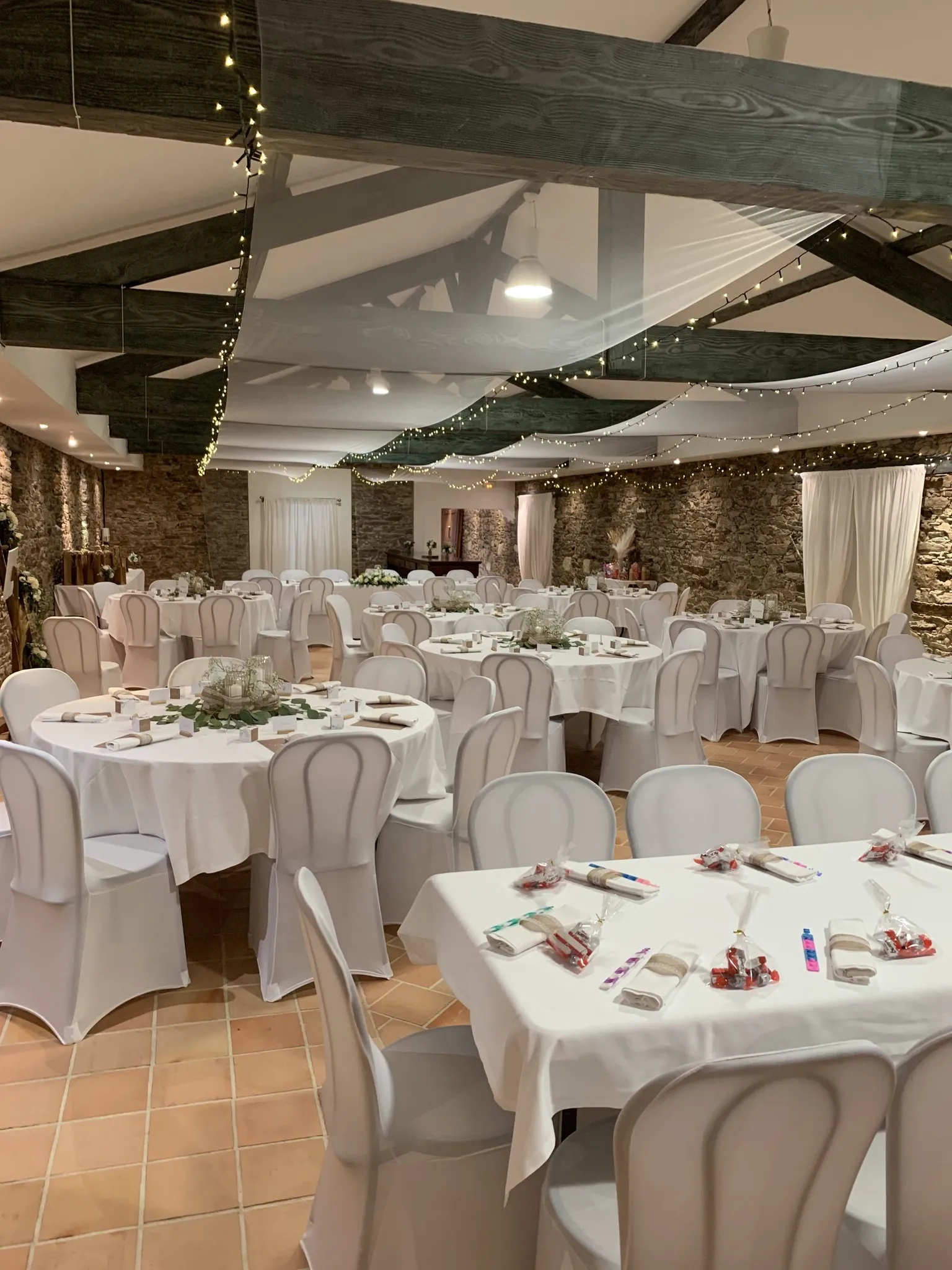 Salle de réception dressée pour un mariage, tables rondes et chaises housses blanches