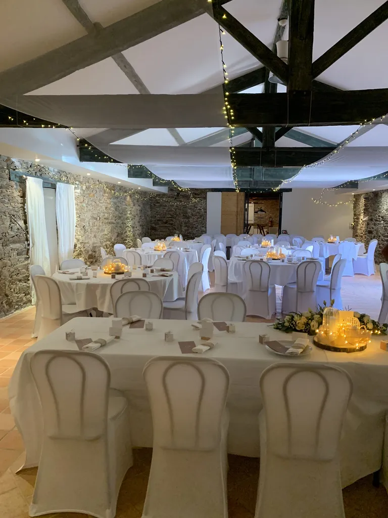 Salle de réception dressée de tables nappées blanches sous la charpente